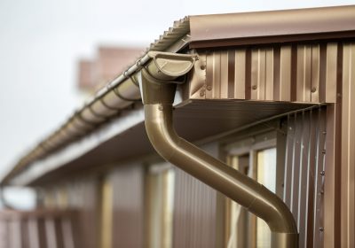 Close-up detail of cottage house corner with metal planks siding and roof with steel gutter rain system. Durability, professional construction, drainage pipes installation and connection concept.
